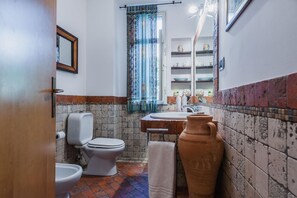 Ein Badezimmer mit Toilette, Bidet und Waschbecken. Ein Handtuchhalter und ein Spiegel befinden sich über dem Waschbecken.