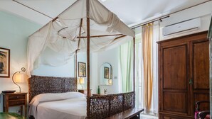 A room with a four-poster bed, a wooden wardrobe, a mirror, and a painting on the wall. - Villa Amun con Giardino by Wonderful Italy (Riposto)