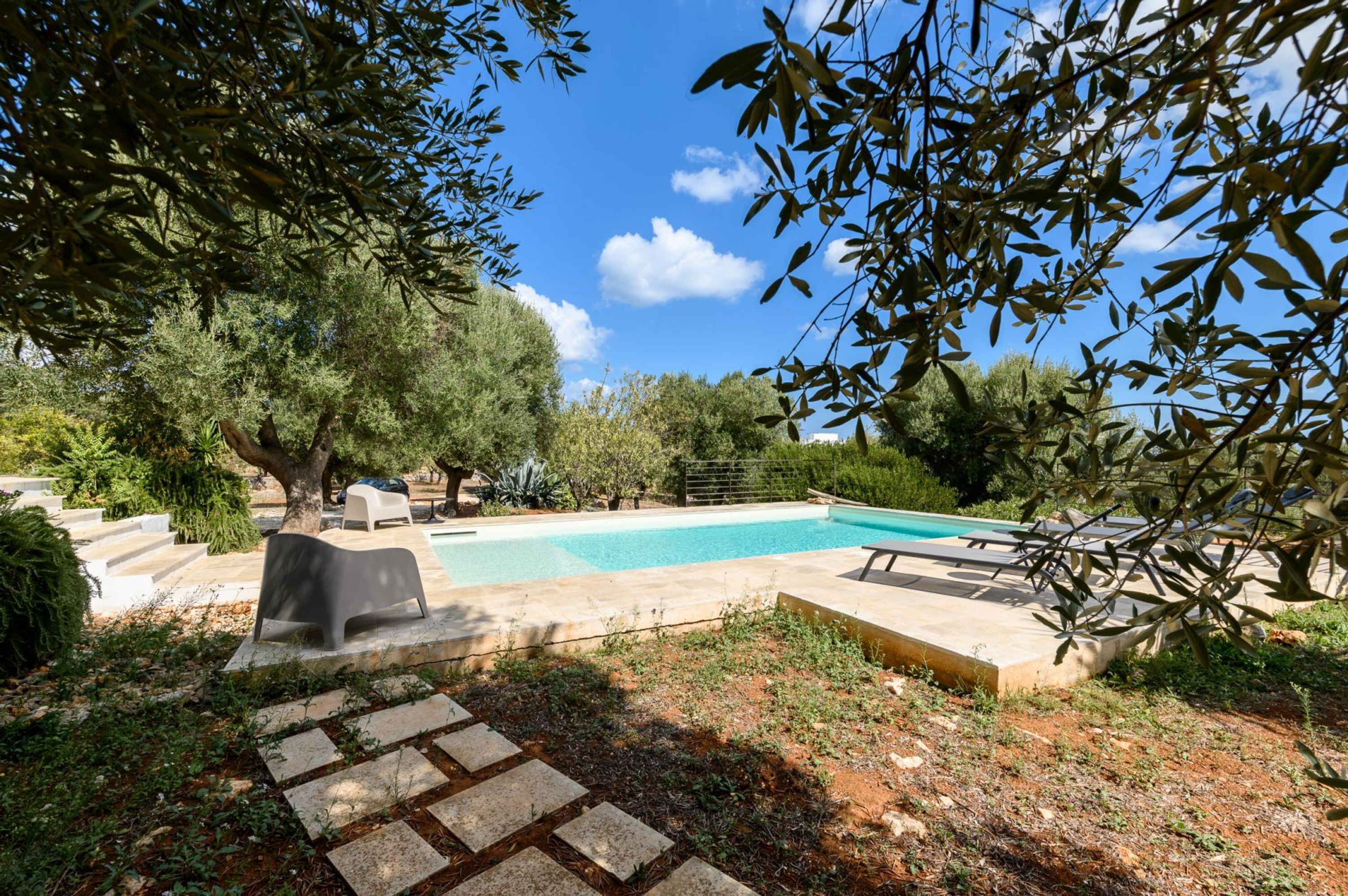 A swimming pool surrounded by stone steps and greenery, with a clear blue sky above.