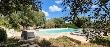 A swimming pool surrounded by stone steps and greenery, with a clear blue sky above.