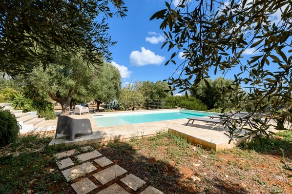 A swimming pool surrounded by stone steps and greenery, with a clear blue sky above.