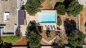 An aerial view of a property with a swimming pool, outdoor seating, and a stone pathway.