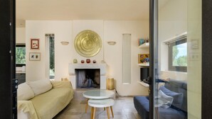 Een woonkamer met een beige bank, een blauwe bank, een open haard en een ronde tafel met houten poten.