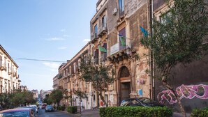 A street view with a building featuring a large arched entrance, balconies, and flags.