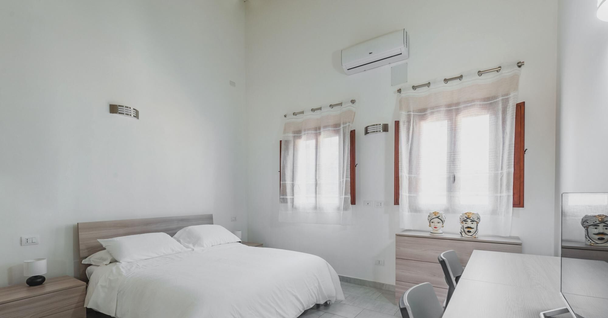 Une chambre d’hôtel propre et moderne, équipée d’un lit simple, d’un bureau avec une chaise et de deux fenêtres avec des rideaux.