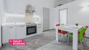 A modern kitchen with white cabinets, a gas stove, and a built-in oven. There is a dining area with a white table and colorful chairs.