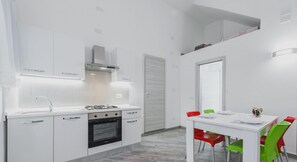 Eine moderne Küche mit weißen Schränken, einem Gasherd und einem eingebauten Backofen. Es gibt einen Essbereich mit einem weißen Tisch und bunten Stühlen.