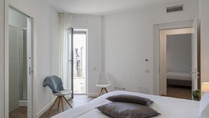 A modern hotel room with a large bed, a chair, and a view of the city through the open door. - Deluxe Apartment - Avio by Wonderful Italy (Genoa)