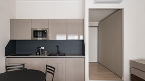 A modern kitchen with a built-in microwave, a coffee machine, and a sink. There is a dining table with chairs and a view of a hallway leading to another room. - Studio Grey al Parco Montagnola by Wonderful Italy (Bologna)