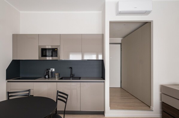 A modern kitchen with a built-in microwave, a coffee machine, and a sink. There is a dining table with chairs and a view of a hallway leading to another room.