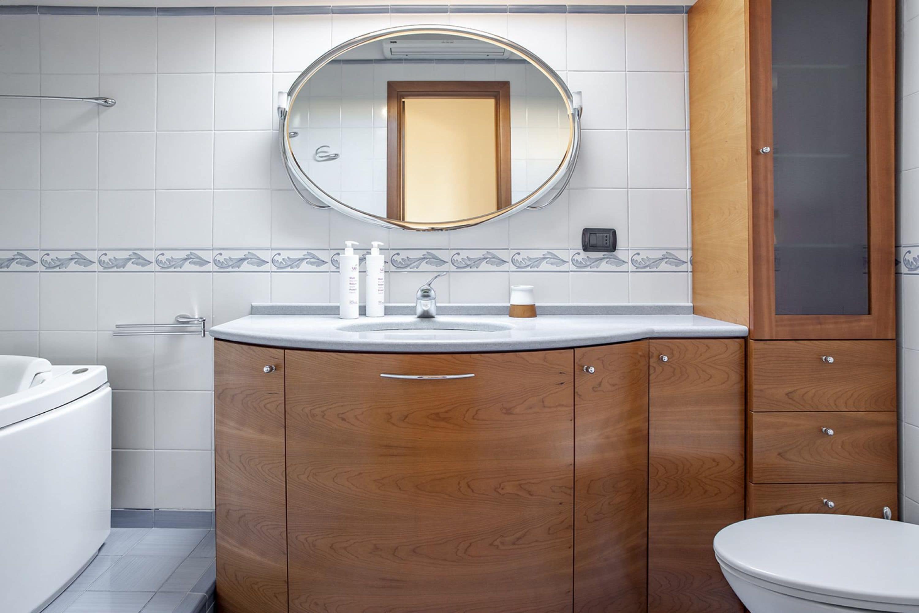 A modern bathroom with a wooden vanity, a round mirror, and a white toilet.