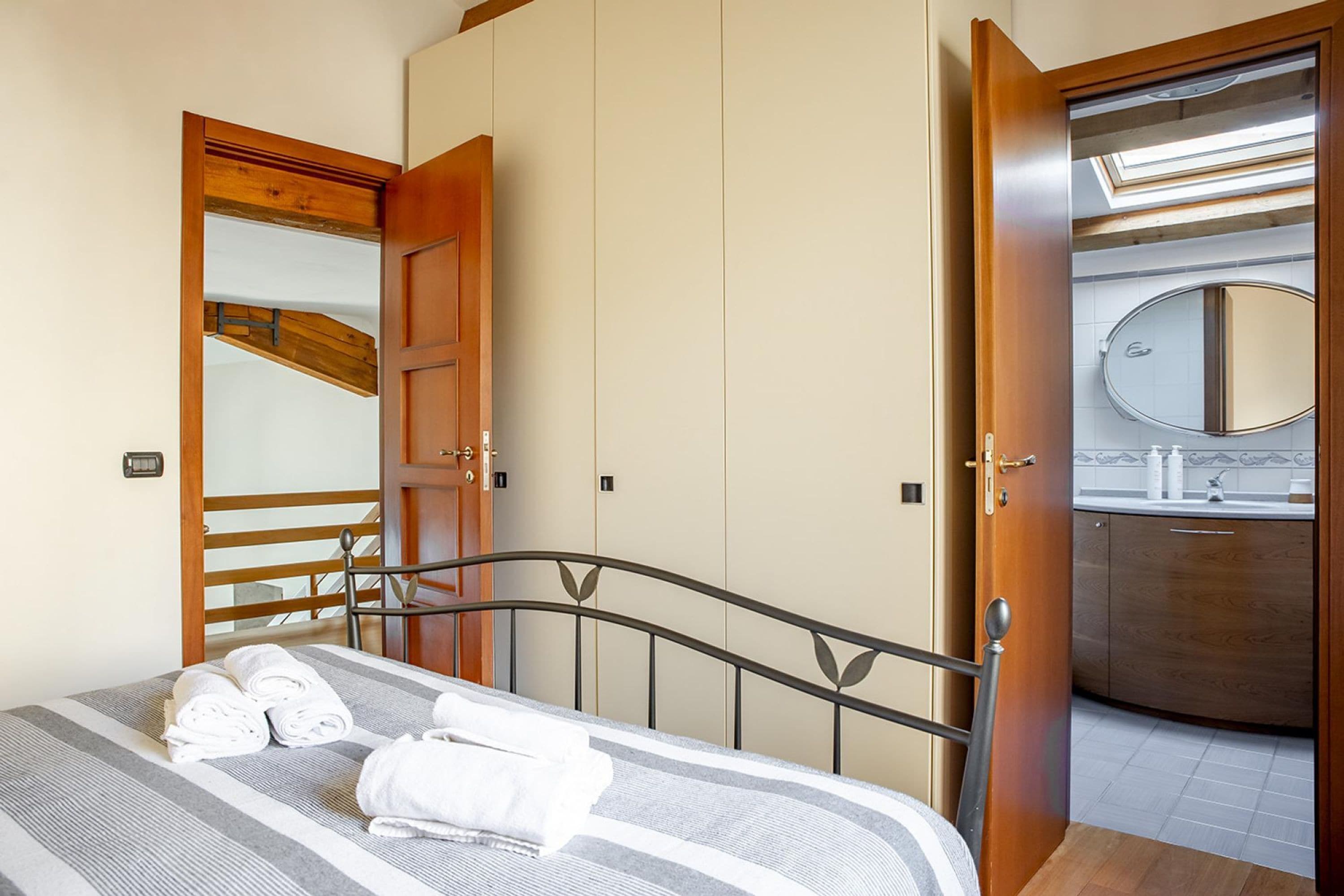 A bedroom with a bed, a wooden wardrobe, a bathroom with a mirror, and a skylight.