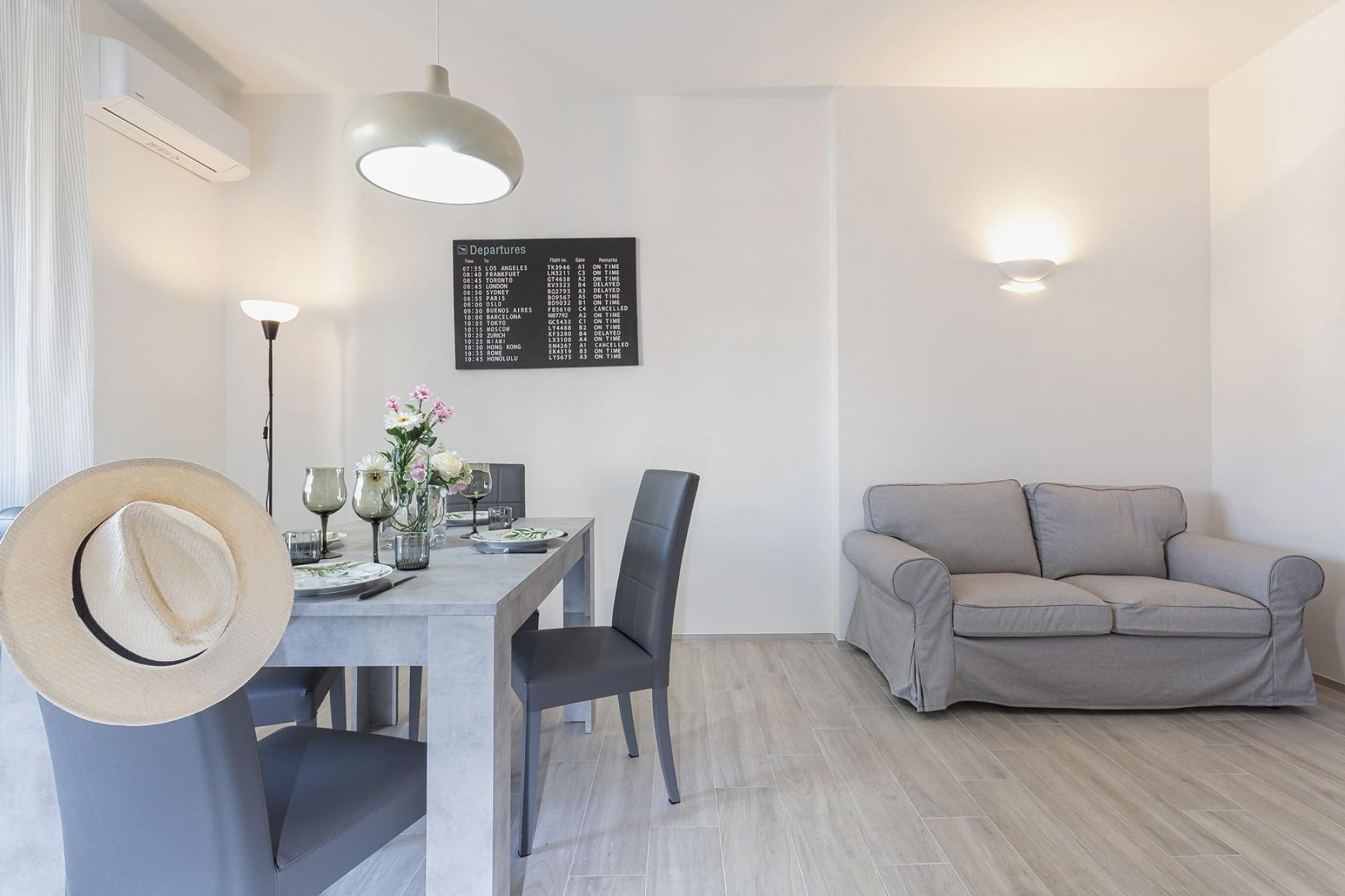 Una sala de estar moderna con comedor, un sofá gris y un panel informativo mural.