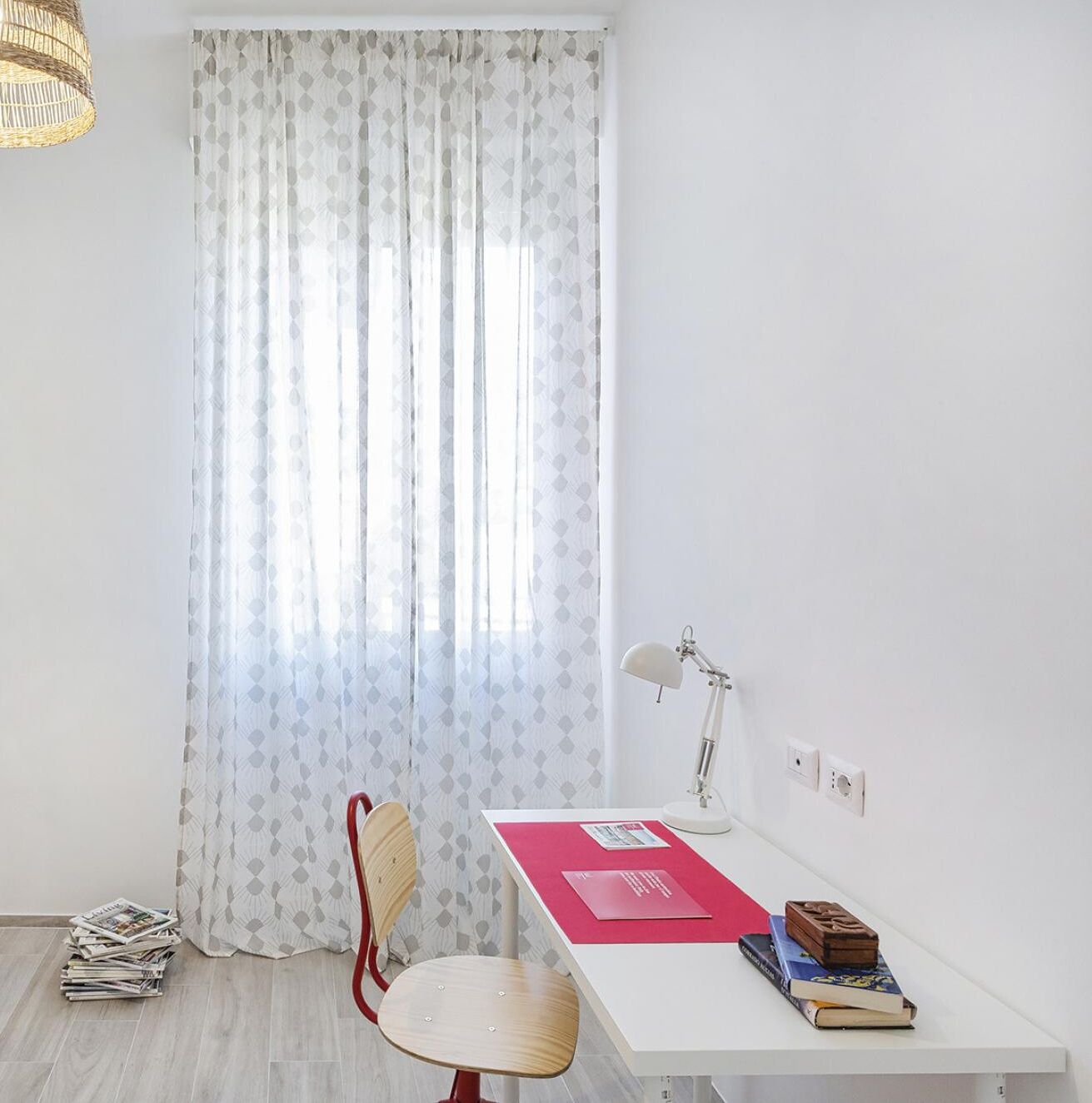 Een kamer met een wit bureau, een stoel, een lamp en een raam met gordijnen met een patroon.