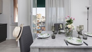 Un coin repas avec une table dressée pour quatre personnes, un vase rempli de fleurs et une vue sur la ville grâce à de grandes fenêtres.