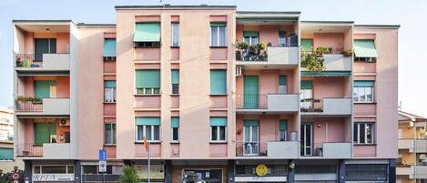 A multi-story residential building with balconies, a parked motorcycle, and a visible storefront with a sign.