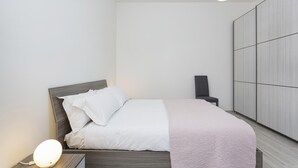 Une chambre à coucher moderne avec un lit bien fait, une table de chevet avec une lampe et une armoire adossée au mur.