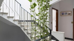 Un escalier avec une rampe métallique, une plante qui pousse le long de la rampe et une porte avec une plaque numérotée.