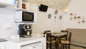 Une cuisine compacte équipée d’un four à micro-ondes, d’une machine à café et d’un réfrigérateur. On y trouve également une table à manger avec des chaises, ainsi qu’un canapé dans le salon attenant.