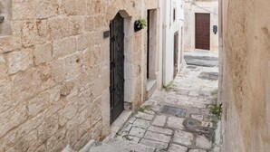 Une ruelle étroite, pavée de pierres, bordée de bâtiments de chaque côté, avec des portes en arc de cercle et un petit seuil menant à une porte.