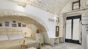 Une chambre avec une arche en pierre, un lit, une table de chevet, une lampe, une petite table avec une lanterne et une porte avec des rideaux.
