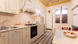 A kitchen with white cabinets, a tiled backsplash, a stove, and a sink. There is a dining table with a plate on it.