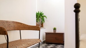 A corner of a room with a wicker chair, a wooden dresser, and a potted plant.