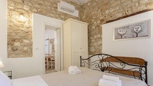 A bedroom with a stone wall, a bed with a metal headboard, a white wardrobe, and a framed artwork on the wall.