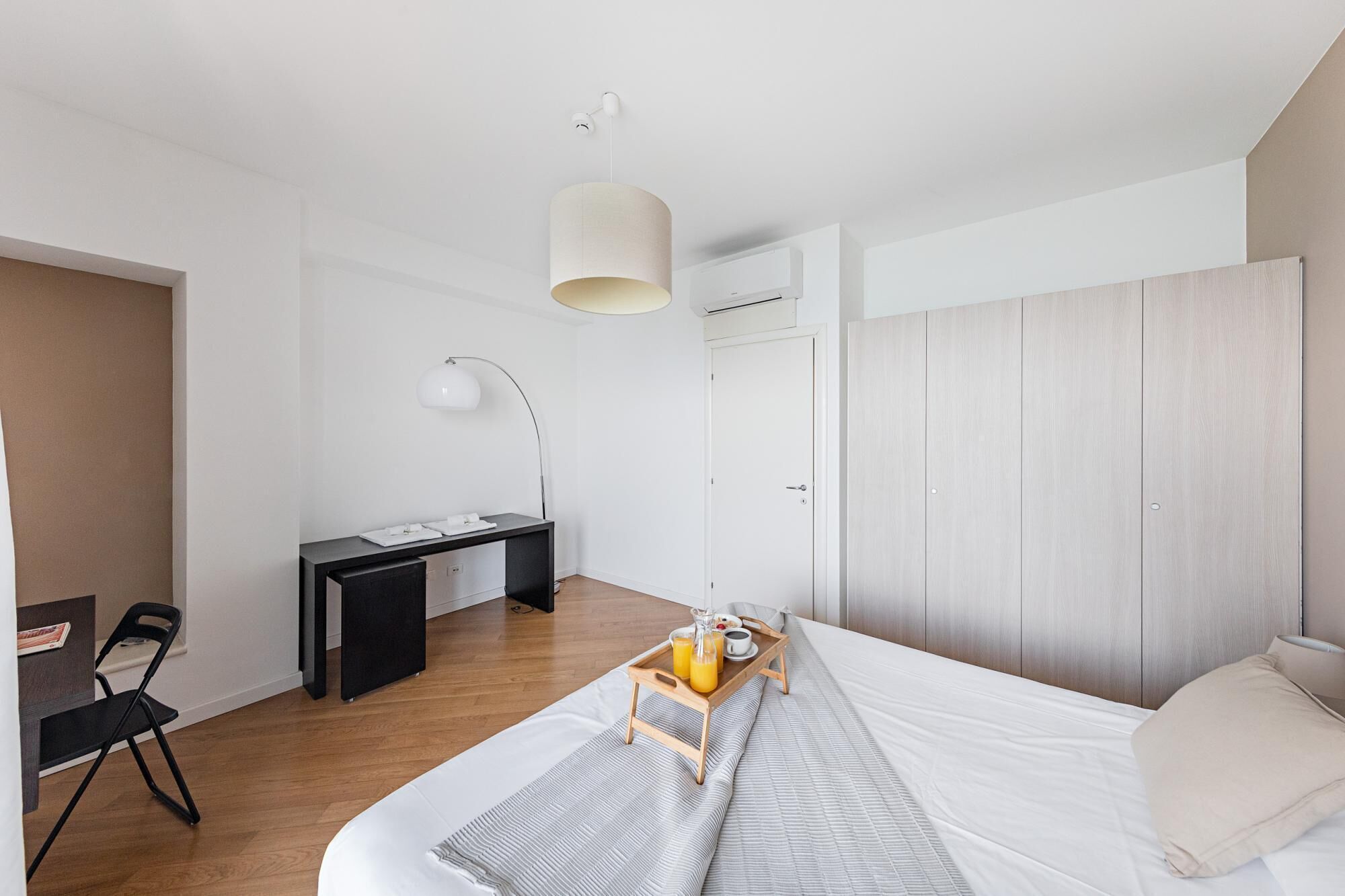 A modern bedroom with a bed, bedside table, desk, chair, and a tray with breakfast.