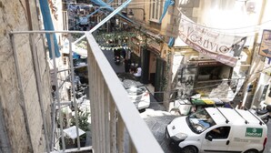 A narrow street with a white van parked on the side, a small shop with a sign, and a building with a balcony. - O Panaro ai Quartieri Spagnoli (Naples)