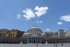 A large open square with a prominent building featuring a central dome and columns, surrounded by other buildings.