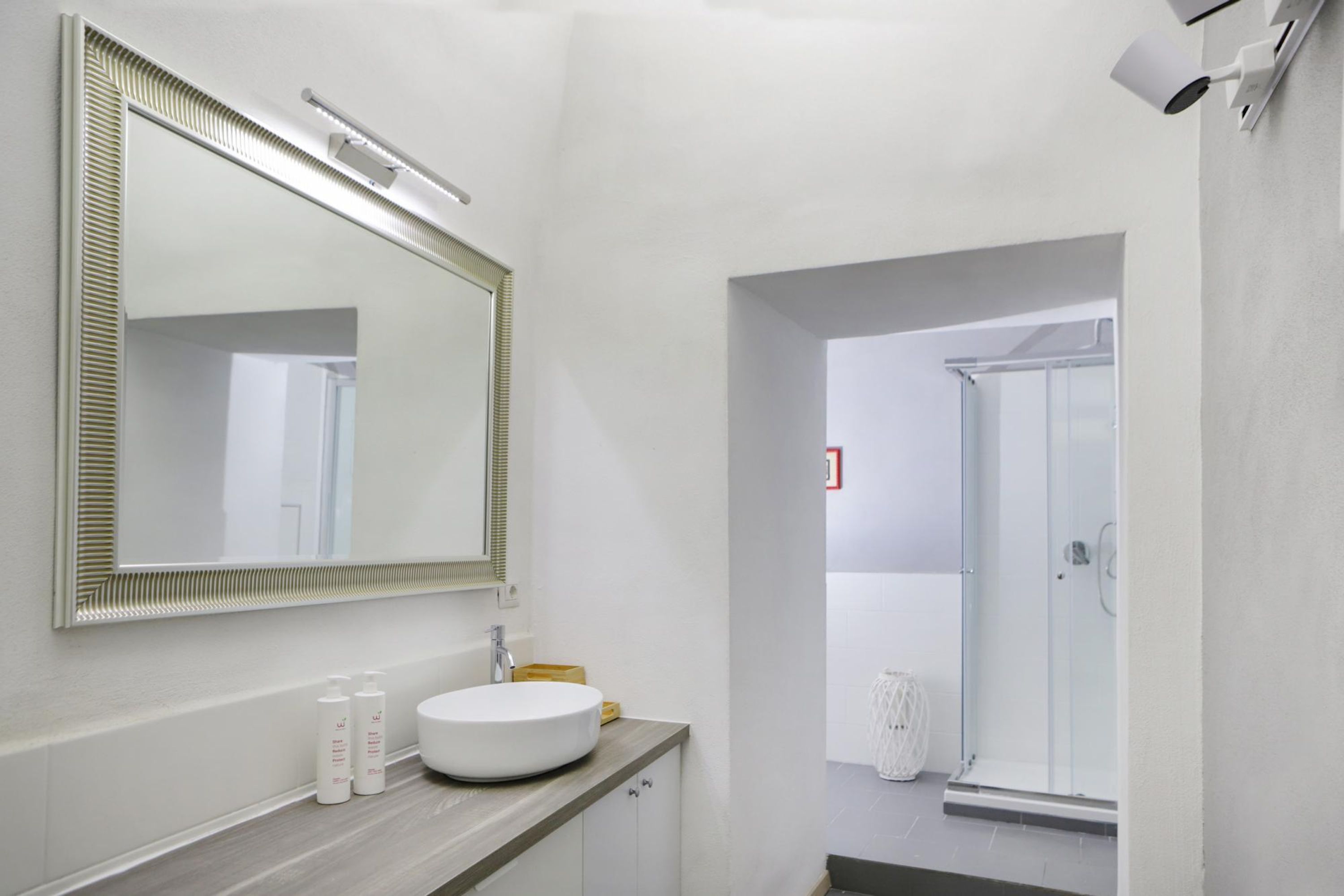 Un bagno moderno con uno specchio grande, un lavandino rotondo e uno spazio doccia visibile attraverso un arco.
