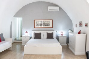 A modern bedroom with a large bed, white nightstands, a dresser, and a framed picture above the bed.
