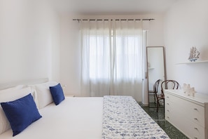 A bedroom with a bed, a nightstand, a dresser, a mirror, and a window with curtains.