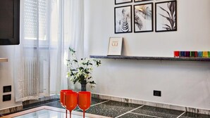 A modern living room with a glass coffee table, a vase with flowers, and a framed picture on the wall.