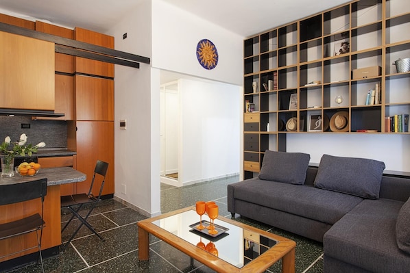 Een moderne woonkamer met een grijze bank, een salontafel en een boekenplank vol boeken en decoratieve objecten.