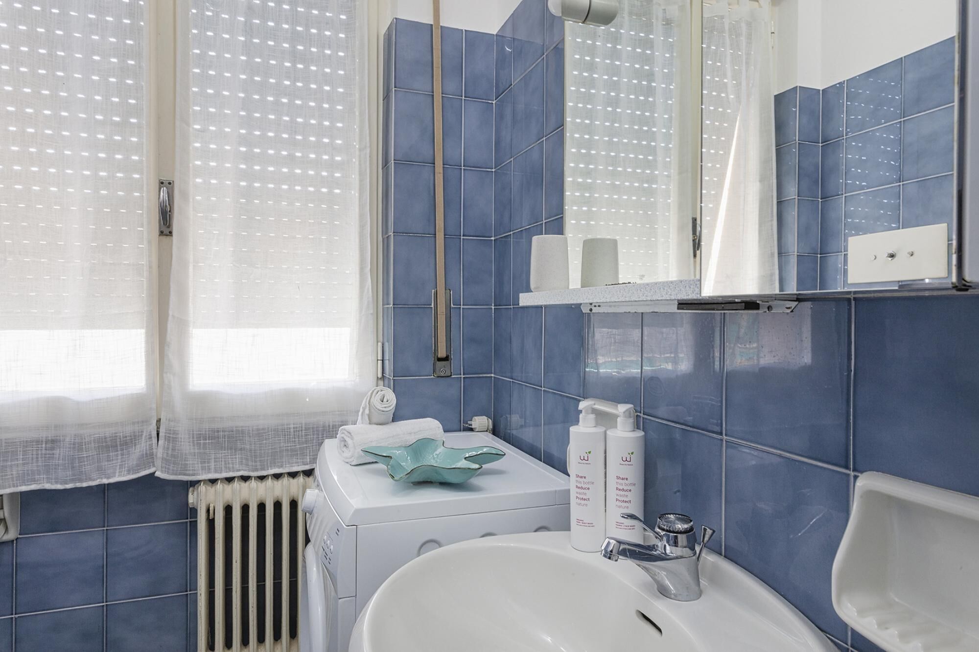 Un baño con un lavabo blanco, azulejos azules, un espejo y una toalla sobre el radiador.