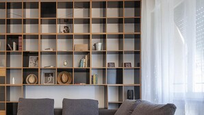 A modern living room with a grey sectional sofa, a glass coffee table, and a wooden bookshelf filled with books and decorative items.
