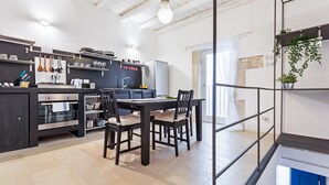 A modern kitchen with a dining area, featuring a black table, chairs, and a hanging light fixture.