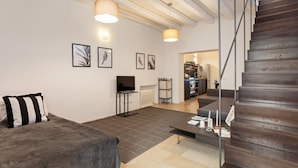 A modern living room with a sofa, a coffee table, and a TV. There is a staircase leading to an upper floor.