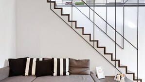 A modern living room with a sofa, a coffee table, and a staircase with a glass railing.