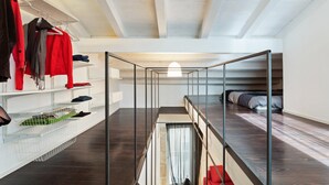A modern loft bedroom with a glass ceiling, a bunk bed, and built-in shelving with clothes and storage bins.