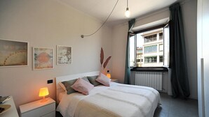 A neatly arranged bedroom with a bed, bedside lamps, and artwork on the walls.
