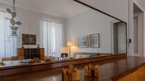 Moderni hotellihuone, jossa on puinen ruokapöytä, sohva ja suuri peili, joka heijastaa huonetta.