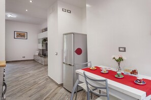 A modern kitchen with a white countertop, a stainless steel refrigerator, and a dining area with a red tablecloth. - La Casa di Lorenzo by Wonderful Italy (Genoa)