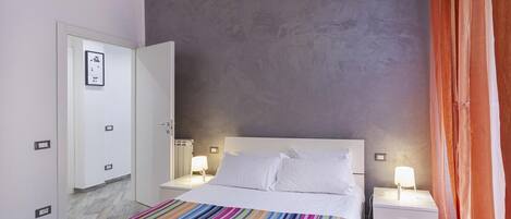 A bedroom with a bed, nightstands, a striped rug, a gray textured wall, and a door with a framed picture.