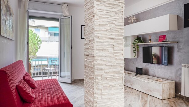 Een moderne woonkamer met een rode bank, een accentmuur van steen, en een keuken met een ingebouwde televisie en witte kasten.
