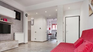 Een moderne woonkamer met een flatscreen televisie, een rode bank en een eethoek op de achtergrond.