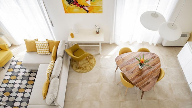 Una sala moderna con un sofá, sillones amarillos, una mesa de comedor con sillas amarillas, una mesa de centro y un cuadro en la pared.