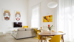 Una sala de estar moderna con un sofá, sillas amarillas, una mesa de comedor de madera y obras de arte en las paredes.